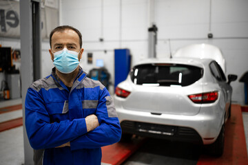 Fototapeta na wymiar Professional caucasian car mechanic wearing protection face mask in vehicle workshop during corona virus pandemic. Covid-19 prevention measures on job.