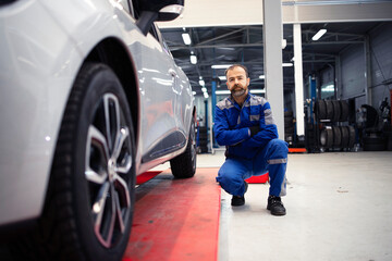 Portrait of professional car mechanic standing in vehicle workshop by an automobile.