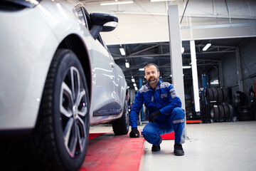 Fototapeta na wymiar Portrait of professional car mechanic standing in vehicle workshop by an automobile.