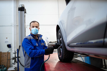 Portrait of professional car mechanic wearing face mask due to corona virus holding pneumatic screw...