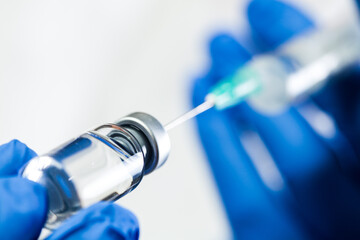 Hand in blue gloves holding syringe with needle inserted into ampoule with antiviral liquid
