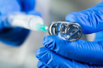 Fototapeta COVID-19 UK vaccine clinical trial concept,hands in blue gloves holding bottle vial obraz