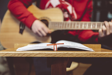 Selective focus shot of a male playing on a guitar with sheet music in front of him