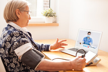 Elderly senior retired woman using sphygmomanometer blood pressure monitor to measure heart rate pulse - obrazy, fototapety, plakaty