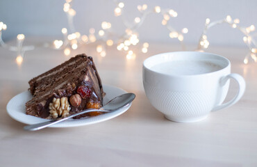 morning coffee in a white mug and a piece of chocolate cake with nuts, on a saucer, on a wooden table, with bokeh in the background. Heavy breakfast, sugar addiction. Allergenic foods, nuts. Homemade