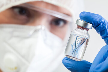 Female NHS microbiologist or lab biotechnician holding glass bottle vial with DNA helix strand...
