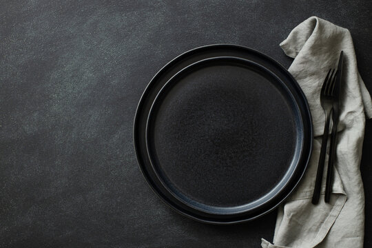 Empty Black Plates With Black Cutlery And Gray Napkin On Black Table. Top View.