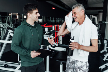 An older man communicates with his coach, they stand in the middle of a modern gym. Sports, health. Rehabilitation specialist, coach