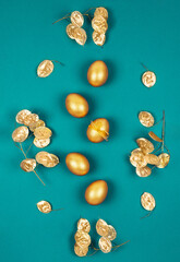 Top view of golden colored Easter eggs with dry flowers over bright green turquoise background. Happy Easter greeting card. Easter wallpaper. Flat lay. Vertical image.