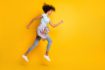 Fototapeta na wymiar Full length photo of charming purposeful dark skin curly girl dressed blue t-shirt jumping running isolated yellow color background