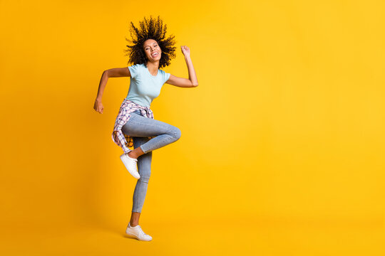 Full length photo of funky pretty dark skin curly girl dressed blue t-shirt dancing empty space isolated yellow color background