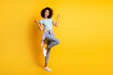 Fototapeta na wymiar Full length photo of lucky dark skin curly woman dressed blue t-shirt rising fists empty space isolated yellow color background
