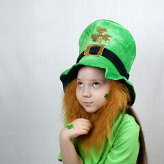 Saint Patricks Day holiday. Portrait of adorable pensive girl with clover leaf on her cheek and...