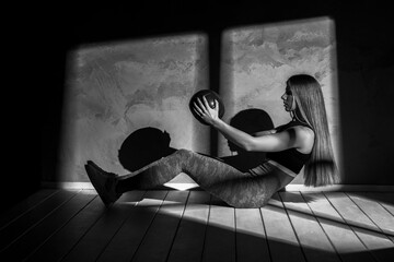 Fit young brunette woman exercise with medicine ball ont in gym on dark background