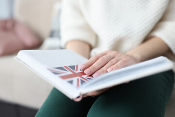 Woman sitting on couch and holding notepad with flag of Britain closeup