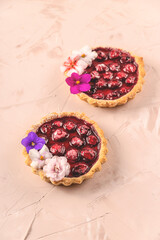 Two spring mini pies with cherry decorated with edible white, pink and purple flowers on pastel background.