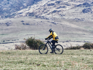 Fototapeta premium Anonymous cyclist dressed in yellow and black with a mountain bike, riding through the fields and mountains