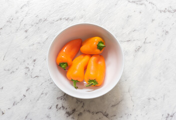 High angle view of orange baby capsicums in white bowl on grey marble effect background (selective focus)