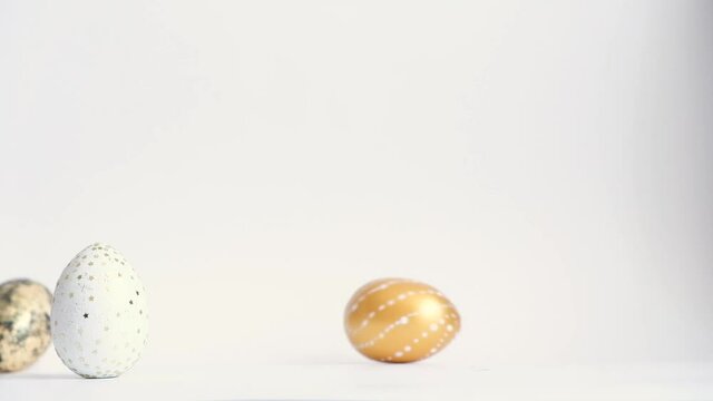 Egg are rolling on the white table, knock each other. Easter golden decorated eggs isolated on white background. Minimal easter concept. Happy Easter card