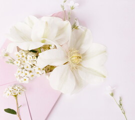 Romantic bouquet of white clematis flowers in a pink envelope, close-up view. Romantic background