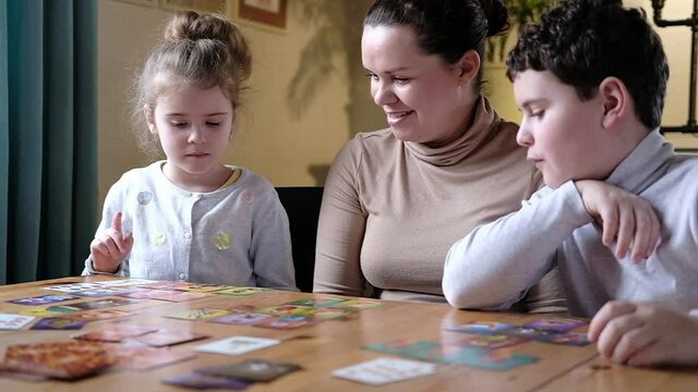 Happy cute kids play board game educational creative dice card game with kids in the bright living room at the table. A fun hobby of a mother with children. family vacation with a board game