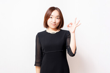 白背景の前に立って、OKのジェスチャーをする喪服を着た女性