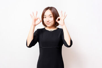 白背景の前に立って、OKのジェスチャーをする喪服を着た女性