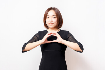 白背景の前に立って、OKのジェスチャーをする喪服を着た女性