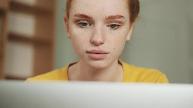 A close-up view of a serious young redhead woman is using her laptop computer while sitting in the office