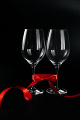 Two empty glasses on the black background with a red ribbon. Composition for Valentine's day. Theme of love banner. Loving, positive emotions. Happy holiday. The concept of celebration and love..