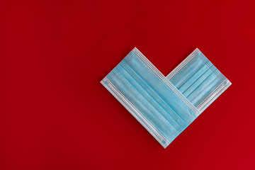 Two close-up blue medical masks stacked in the shape of a heart in red background with space for text. Theme of love banner. Loving, positive emotions. The concept of celebration and love..