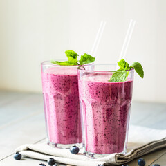 Two glasses of blueberry smoothie with mint garnish and straw on the table. Close up.