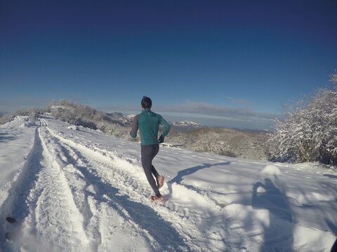 Young Guy Running In A Sunny Winter Day, In Snowy Mountains