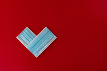 Two blue medical masks stacked in the shape of a heart in red background with space for text. Theme of love banner. Loving, positive emotions. The concept of celebration and love..