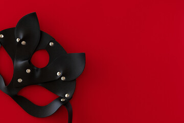 Black leather sexy cat mask on a red background with space for text. Concept of Valentine's Day. Copy space, top view. The concept of Valentine's Day. Theme of love banner. Loving, positive emotions