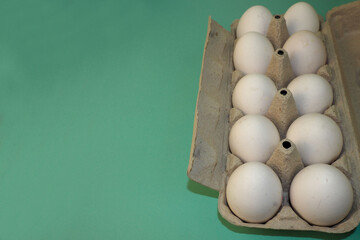 ten white raw eggs in a cardboard box on a green background side view