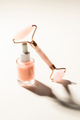 Rose serum bottle  and Gua Sha massage rolleron white vackground with shadow for natural skin care routine concept.
