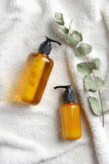 Yellow dispenser bottles and eucalyptus leaf on white towel in bathroom. SPA natural organic cosmetics set.