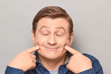 Portrait of cheerful man touching cheeks with fingers and smiling