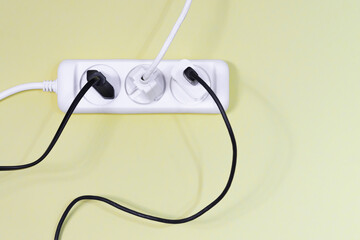 A mess of white and black electrical wires from the extension cord. Electrical wires and chargers close up on a yellow background. The concept of information overload