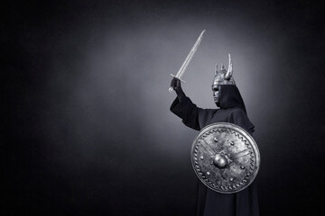 Scary figure with horned helmet, sword and round shield in the dark