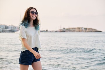 Beautiful teenager girl in sunglasses with dyed blue hair on sea beach, copy space