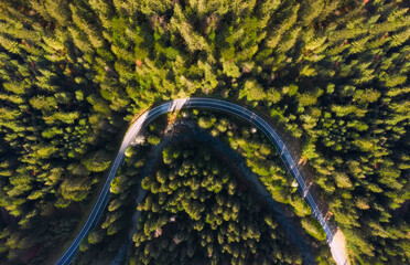 Aerial view of the road in the forest from above. The road goes around a mountain river.