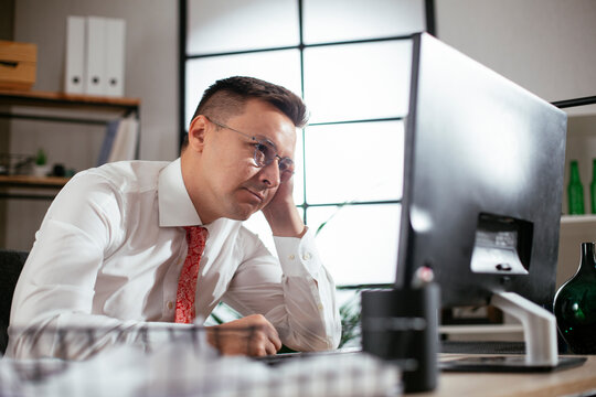 Exhausted businessman working on computer in the office. Tired man sitting at office desk working on computer.
