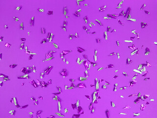 Confetti foil pieces on purple background. Abstract festive backdrop.