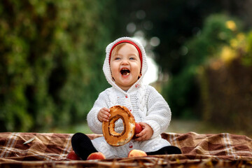 Little girl eating a bagel in the park sitting on a blanket - obrazy, fototapety, plakaty