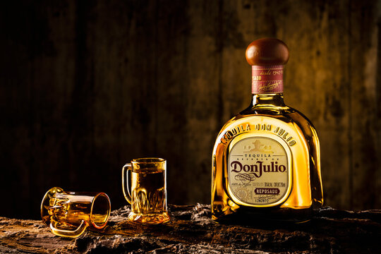 Bottle of Mexican tequila called Don Julio accompanied by two glasses of tequila on a tree bark in a rustic wooden setting. Illustrative editorial photography