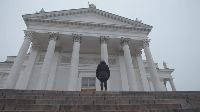 Tracking shot of single person standing at the top of the steps in front of Helsinki Cathedral
