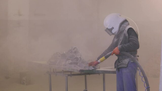 The man is sandblasting the detail. Sandblast metal parts. Sandblasting gun