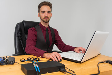 young handsome man with a beard in a bright room sitting at a table, working, on the table are...